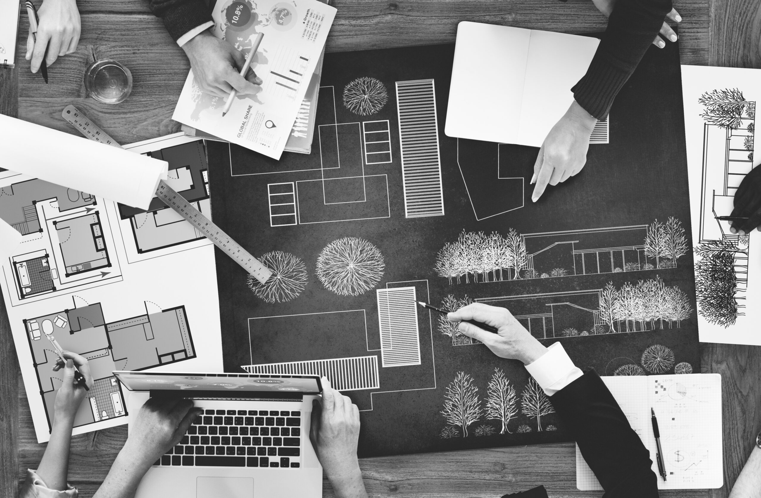 Group of landscape designers collaborating on project plans, featuring sketches of outdoor spaces, a laptop, and design tools, emphasizing professional landscape design for residential projects.