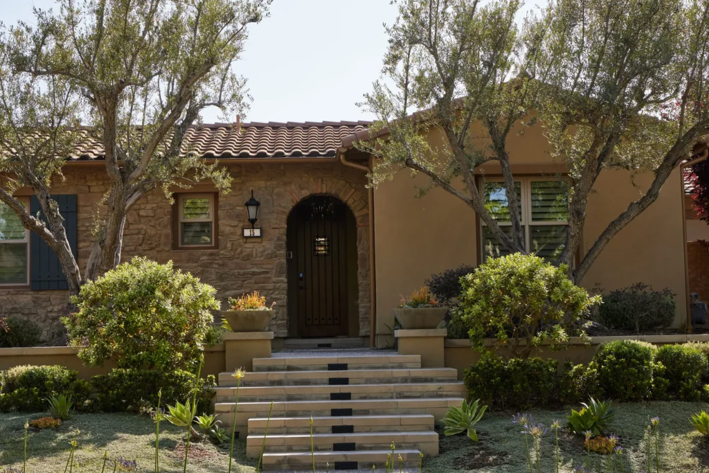 Residential home exterior with stone facade, decorative landscaping, and softscape design featuring shrubs and trees, enhancing urban outdoor space aesthetics.