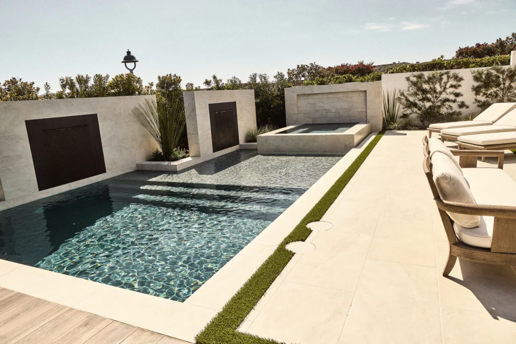 Luxury backyard pool with modern design, sleek stone walls, and comfortable lounge chairs, showcasing an elegant outdoor living space ideal for relaxation and entertainment.